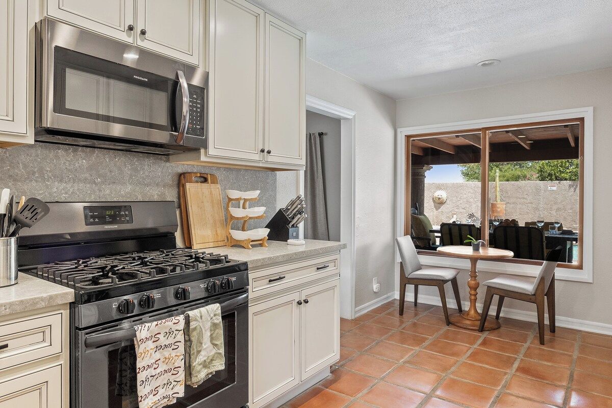 A kitchen with a stove, microwave, and cabinets, a dining area with chairs and a table, and a view through a window.