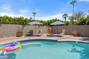 A swimming pool with lounge chairs and umbrellas, surrounded by a low wall and greenery. - Vista El Quetzal - Central Palm Springs (Palm Springs)