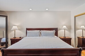 A neatly made bed with a wooden headboard, two bedside tables with lamps, and a large mirror on the wall. - Vista El Quetzal - Central Palm Springs (Palm Springs)