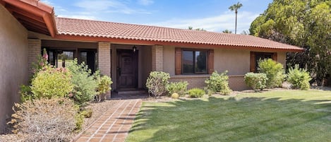 A single-story house with a red-tiled roof, a brick exterior, and a well-maintained lawn.