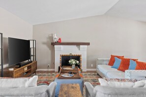 A living room with a flat-screen TV, a fireplace, a sofa, and a coffee table. - Vista El Quetzal - Central Palm Springs (Palm Springs)