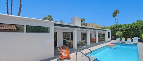 A modern pool area with a clear blue pool, lounge chairs, and a patio with outdoor seating.