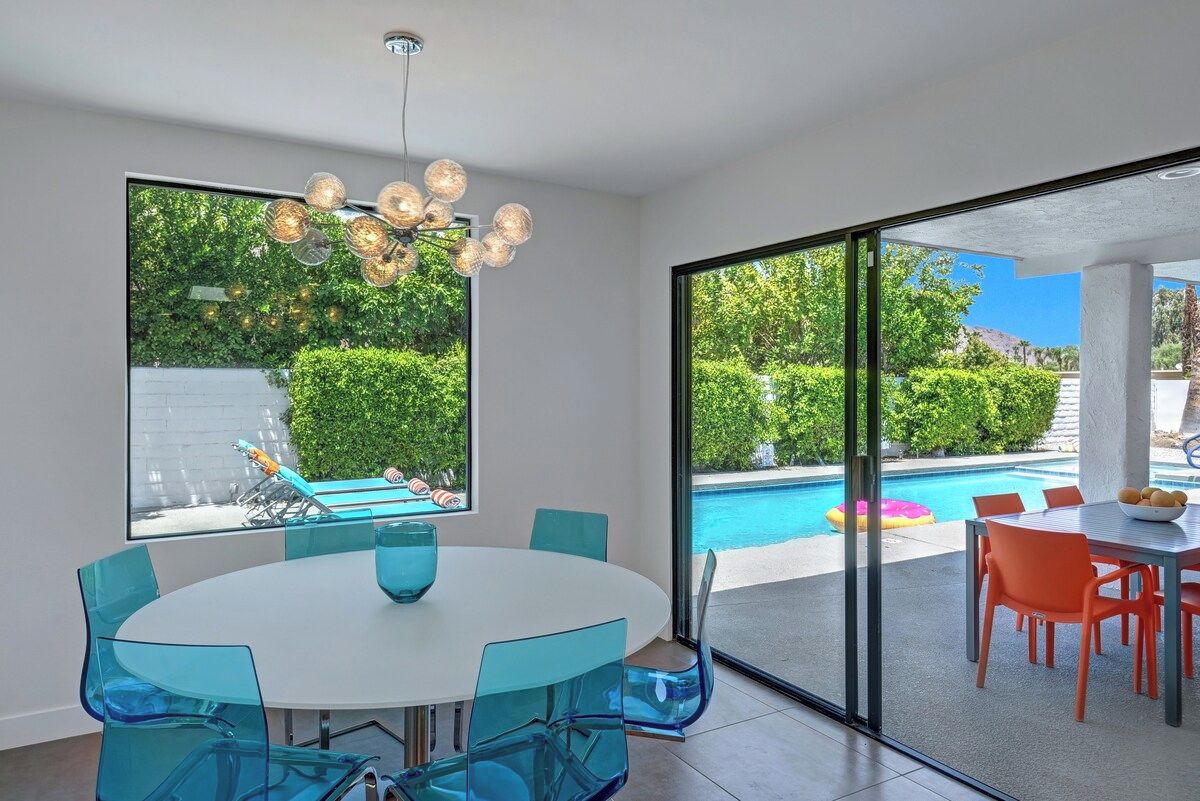 Un comedor moderno con una mesa redonda y sillas, ventanas amplias con vistas a una piscina y vegetación.
