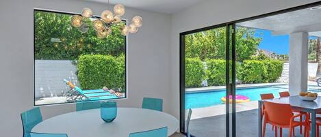 Un comedor moderno con una mesa redonda y sillas, ventanas amplias con vistas a una piscina y vegetación.