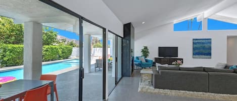 A modern living room with a pool view, a sofa, a TV, and a dining area with chairs.
