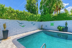 A swimming pool with a white brick wall, green decorative elements, and potted plants. - Luxury Deepwell Stunner (Palm Springs)