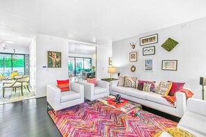 A modern living room with a white sofa, colorful rug, and various wall art. - Luxury Deepwell Stunner (Palm Springs)
