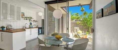 Una cocina moderna con muebles blancos, una mesa de comedor de vidrio y vistas al exterior.