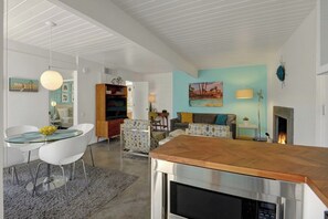 Ein modernes Wohnzimmer mit einem Glastisch, weißen Stühlen, einem Holztisch, einem Kamin und einem Gemälde an der Wand.