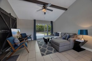 A modern living room with a ceiling fan, a grey sofa, blue armchairs, a coffee table, and a side table with a lamp. - Vista Ranch Hideaway: Palm Springs Home with Private Pool and Mountain Views (Palm Springs)