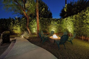 An outdoor seating area with a fire pit and chairs, surrounded by trees and a grill. - Vista Ranch Hideaway: Palm Springs Home with Private Pool and Mountain Views (Palm Springs)
