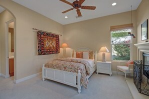 A bedroom with a bed, bedside tables, a ceiling fan, a window with a view, and a decorative tapestry. - PGA West Paradise by Oranj Palm (La Quinta)