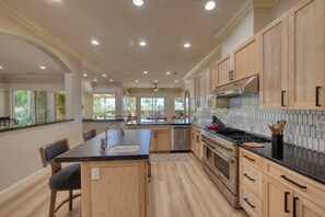 Une cuisine moderne avec des meubles en bois, un îlot central, des appareils électroménagers en acier inoxydable et une vue sur l’extérieur.