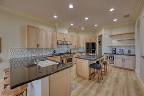 A spacious kitchen with wooden cabinets, a central island, and a breakfast bar. - PGA West Paradise by Oranj Palm (La Quinta)