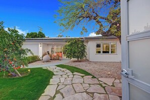 A modern house with a stone pathway leading to the entrance, surrounded by well-maintained greenery and a clear blue sky. - Casa San Lucas - Central Palm Springs (Palm Springs)