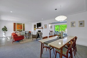 A modern living room with a red sofa, a dining table with chairs, a TV, and artwork on the walls. - Casa San Lucas - Central Palm Springs (Palm Springs)
