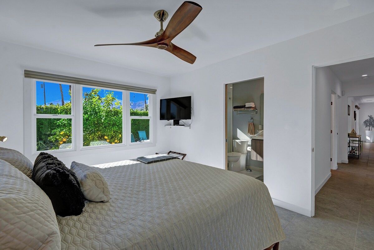 Une chambre à coucher avec un lit, un ventilateur de plafond, une télévision et une fenêtre donnant sur un paysage verdoyant.