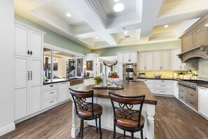 A spacious kitchen with white cabinetry, a central island with two chairs, and a large stove. - Casa Sueños - Andreas Hills (Palm Springs)