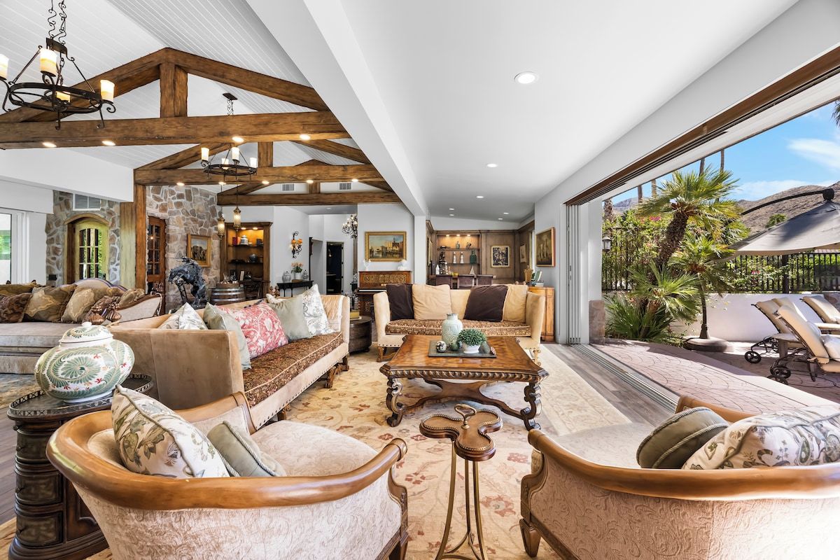 A spacious living room with a high ceiling, wooden beams, and a view of a landscaped outdoor area.