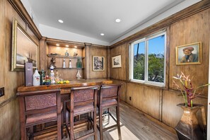 A kitchen with wooden paneling, a bar area with stools, and a window with a view of greenery. - Casa Sueños - Andreas Hills (Palm Springs)