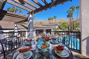 A dining table set with plates, glasses, and a pitcher, overlooking a swimming pool and palm trees. - Casa Sueños - Andreas Hills (Palm Springs)