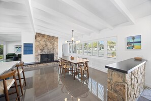 A modern kitchen with a stone accent wall, a dining area with wooden chairs, and a large window with a view. - Sun & Stone Retreat (Palm Springs)