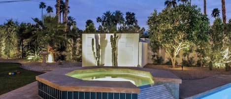A hot tub with a tiled surround, a small pool, and a landscaped garden with palm trees.