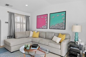 A modern living room with a sectional sofa, a glass coffee table, and artwork on the wall. - Mesquite WorkPlay Oasis - Central PS (Palm Springs)