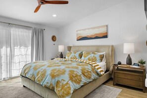 Un dormitorio con cama, mesitas de noche, ventilador de techo, un cuadro y una ventana con cortinas.