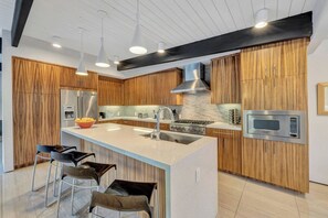 Eine moderne Küche mit Holzausstattung, Edelstahlgeräten und einer zentralen Kochinsel mit Barhocker.