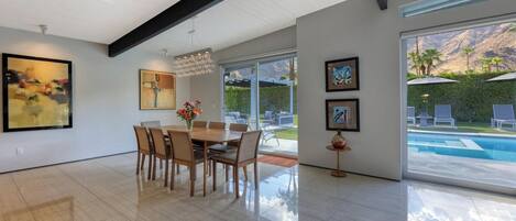 A spacious dining area with a large table and chairs, a chandelier, and artwork on the walls.