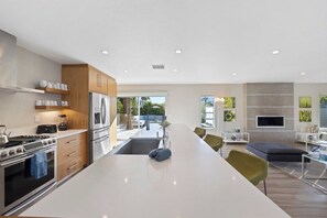 Een moderne keuken met een centraal eiland, roestvrijstalen apparatuur en een eethoek met een groot raam.
