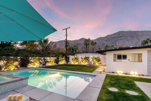 A modern house with a swimming pool, a well-maintained lawn, and a mountain backdrop. - Retreat on Mesquite - South PS (Palm Springs)