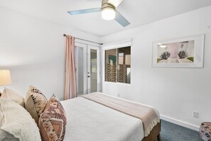A bedroom with a bed, a ceiling fan, a window with a view, and a framed picture on the wall. - Retreat on Mesquite - South PS (Palm Springs)
