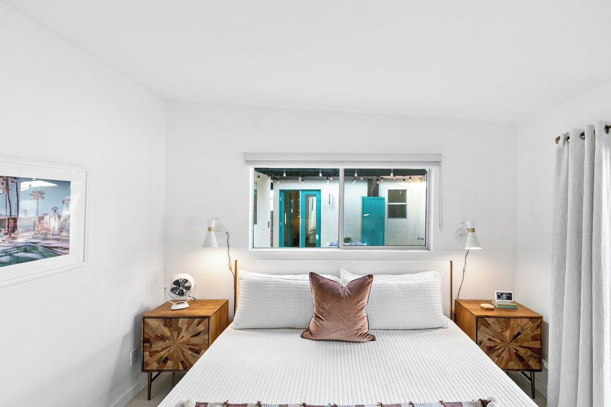 A bedroom with a bed, two bedside tables, a window, and a view of the bathroom.