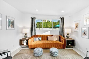 A modern living room with a sofa, two side tables, a rug, and a window with curtains. - Retreat on Mesquite - South PS (Palm Springs)