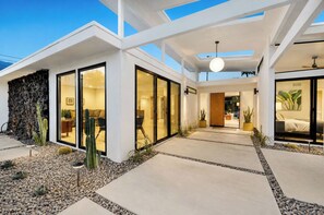 A modern house with large glass doors, a patio with plants, and a clear sky. - Casa Roka - Luxury 4 Bedroom Palm Springs Retreat with Private Pool and Hot Tub (Palm Springs)