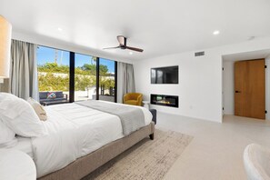 Ein modernes Schlafzimmer mit einem großen Bett, einem Deckenventilator, einem an der Wand montierten Fernseher und Blick ins Freie.