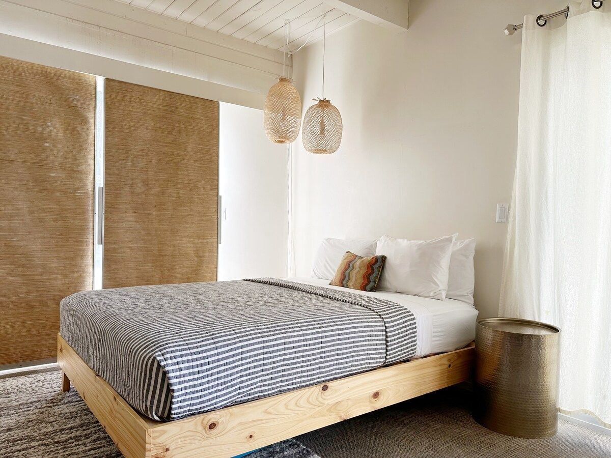 A bedroom with a wooden bed frame, a striped bedspread, and two hanging light fixtures.