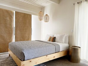 Un dormitorio con cabecera de cama de madera, edredón a rayas y dos lámparas colgantes.