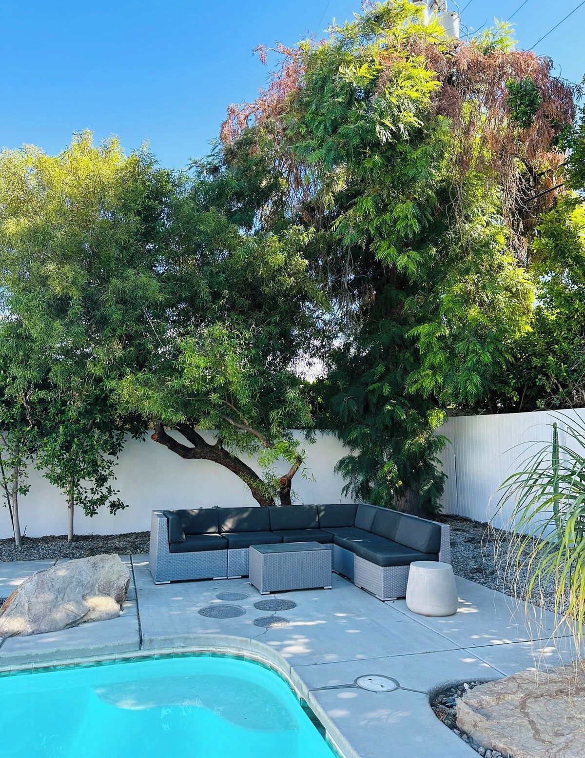 A poolside area with a built-in seating arrangement and a tree providing shade.