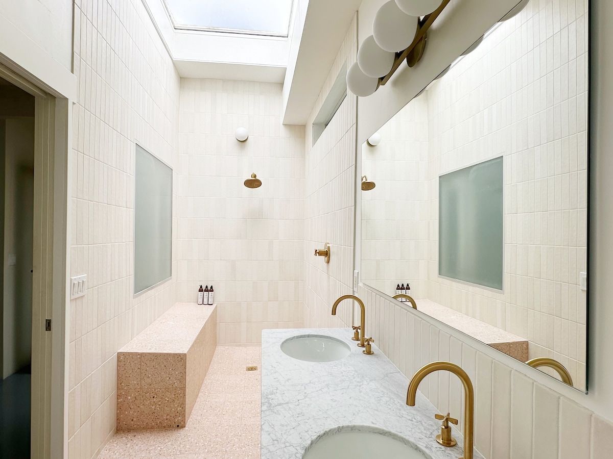 Ein modernes Badezimmer mit zwei Waschbecken, einem großen Spiegel und einem Oberlicht.