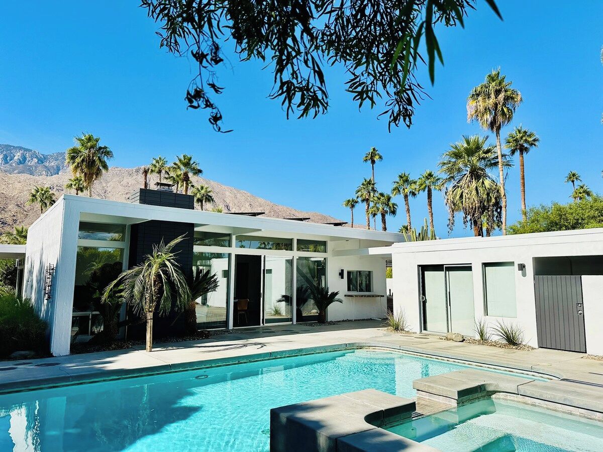 Ein modernes Haus mit Swimmingpool, Palmen und einem Berg im Hintergrund.