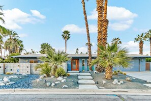 A modern building with a blue facade, a red door, and a paved driveway leading to a garage. - Sunrise Paradise: Palm Springs Home with Private Pool and Mountain Views (Palm Springs)
