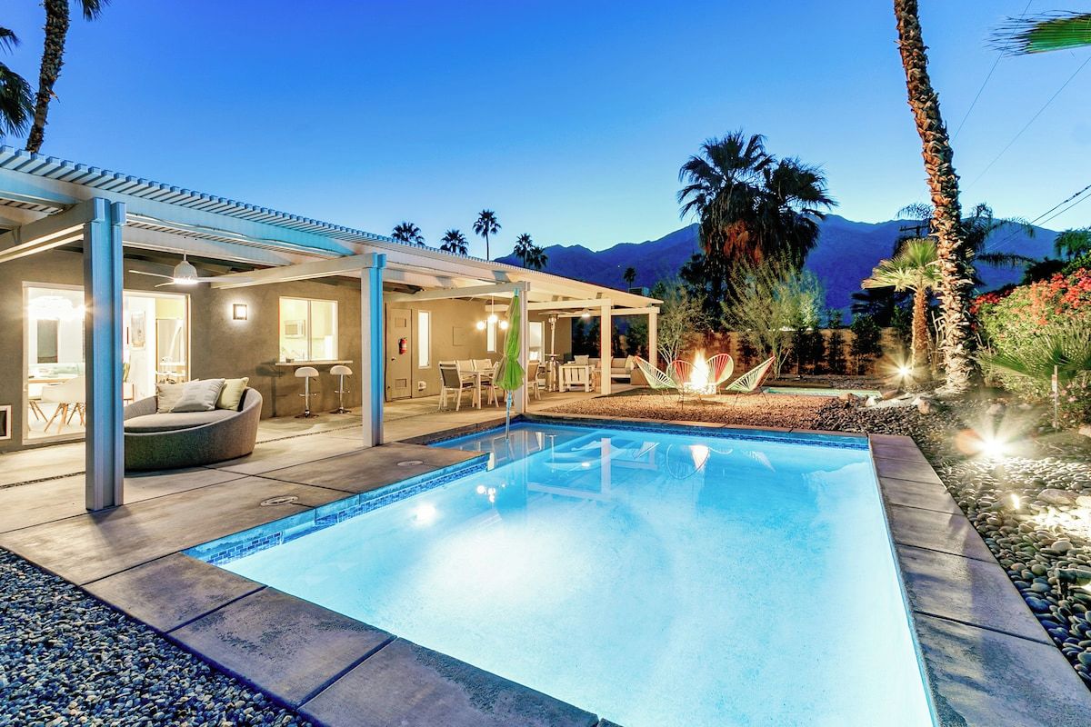 A swimming pool with a covered patio area, outdoor furniture, and a view of mountains.