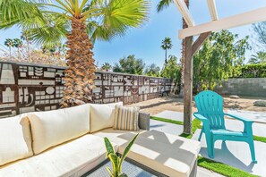 An outdoor seating area with a white sofa, a striped pillow, and a blue chair. - Dreamville Palm Springs by Oranj Palm (Palm Springs)