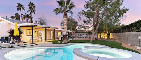 Piscina residencial con jacuzzi, rodeada de césped y árboles.