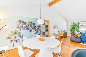 A modern living space with a round dining table, white chairs, a blue sofa, and a large window. - Dreamville Palm Springs by Oranj Palm (Palm Springs)