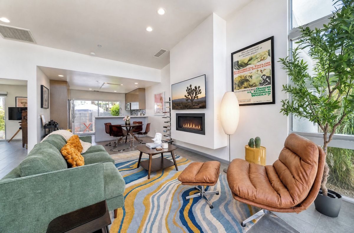 Un salon moderne avec un canapé, un fauteuil et une cheminée. On aperçoit à l’arrière-plan un coin repas avec une table et des chaises.