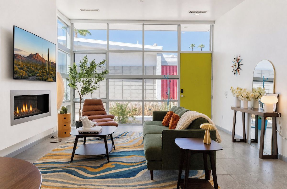 Un salon moderne avec une cheminée, un canapé vert, une table basse et une grande fenêtre donnant sur l’extérieur.